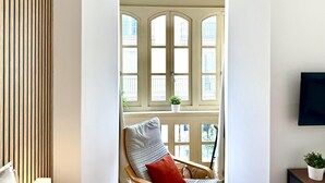 A room with a wooden slat wall, a chair with a cushion, a small table with a plant, and a window with multiple panes. - EL BALCÓN MÁLAGA MALAGA (MALAGA)