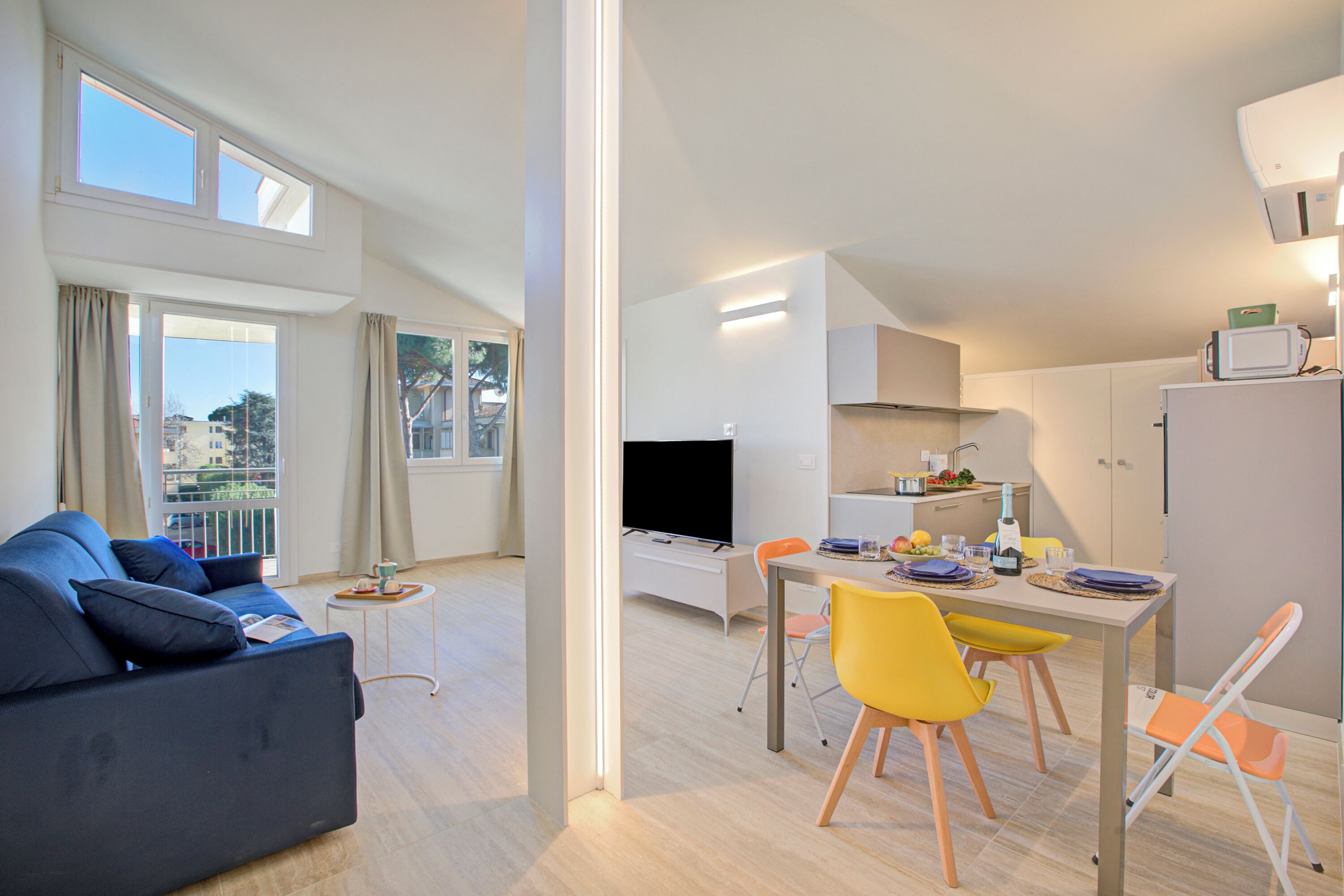 A modern apartment with a living room, dining area, and kitchen. It features a sofa, dining table, chairs, a TV, and a refrigerator.