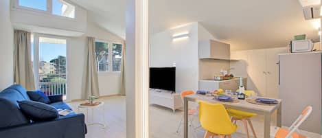 Un apartamento moderno con sala de estar, comedor y cocina. Cuenta con un sofá, una mesa de comedor, sillas, un televisor y un refrigerador.