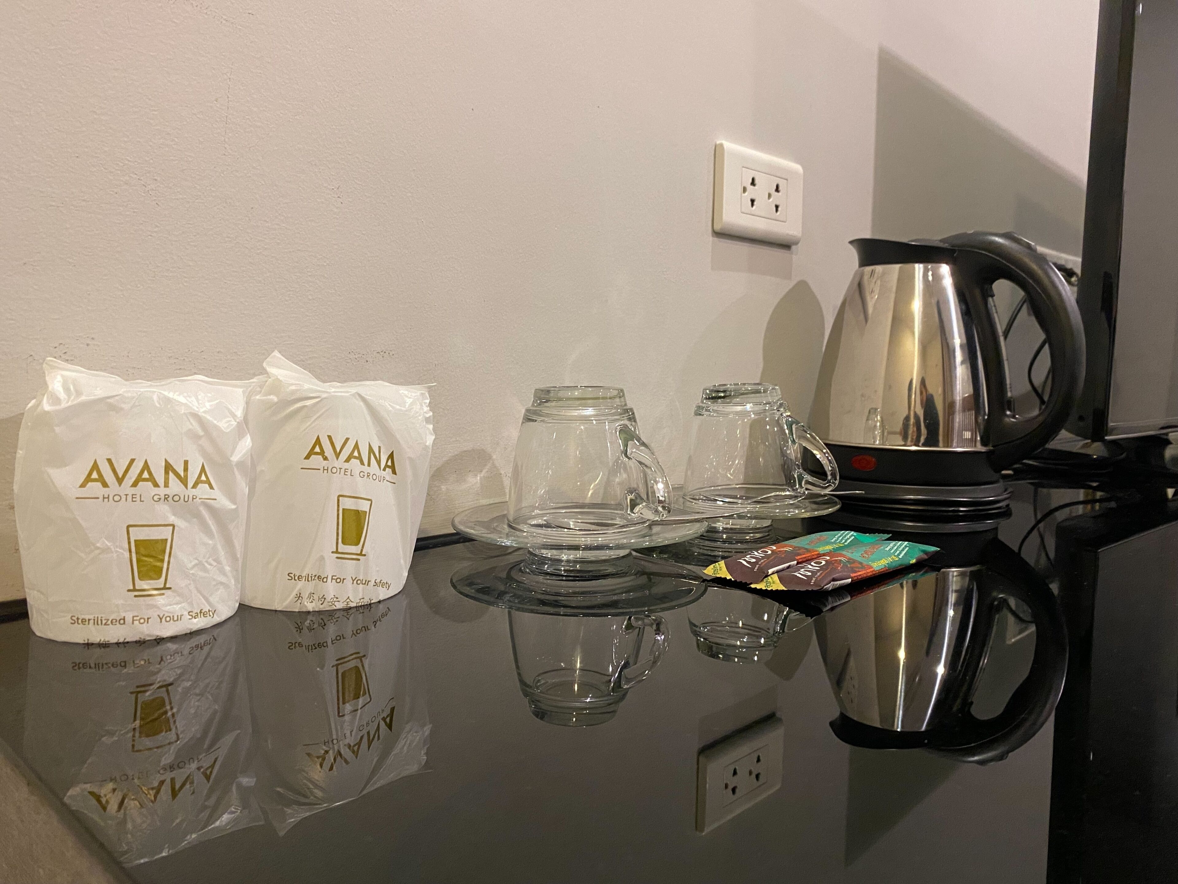 Una habitación de hotel con una mesa preparada para tomar té, dos bolsas con la etiqueta 'AVANA HOTEL GROUP' y un hervidor.