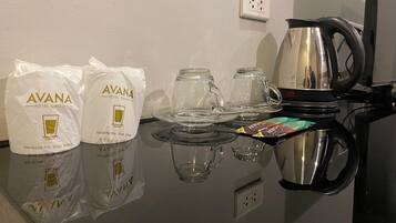 Una habitación de hotel con una mesa preparada para tomar té, dos bolsas con la etiqueta 'AVANA HOTEL GROUP' y un hervidor.