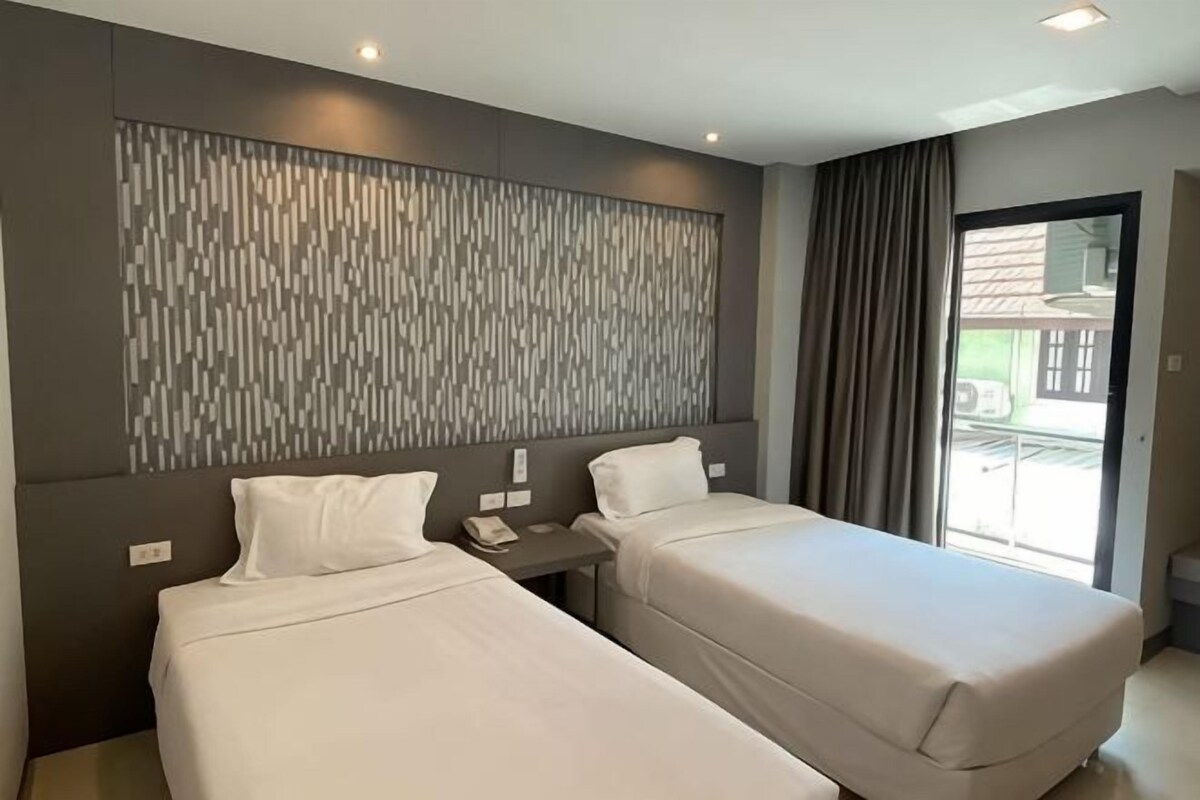 Une chambre d’hôtel avec deux lits, une grande fenêtre, un panneau lumineux fixé au mur et une porte coulissante donnant sur l’extérieur.