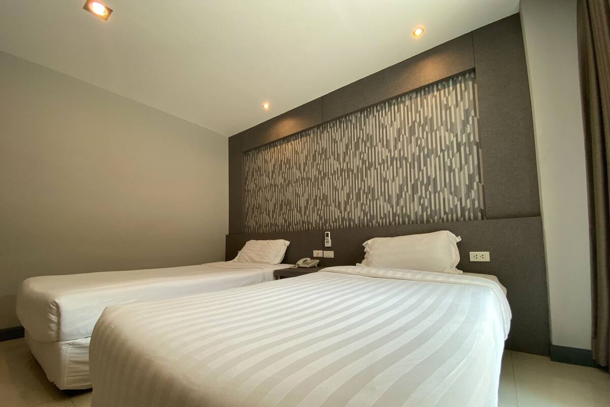 Ein Hotelzimmer mit zwei Einzelbetten, einem modernen Kopfteil und einem an der Wand befestigten Telefon.