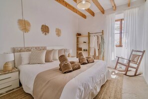A bedroom with a wooden bed frame, a wooden rocking chair, a bedside table with a lamp, and a window with curtains. - Llampí, Nature, swimming pool and Mallorcan charm (Maria De La Salut)