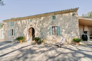 A stone building with a rustic appearance, featuring a wooden door, green shutters, and potted plants. - Llampí, Nature, swimming pool and Mallorcan charm (Maria De La Salut)