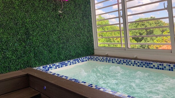 A spa area with a hot tub, a green wall, and a window with a view of trees. - Charming Getaway in the Heart of Baní – Private Jacuzzi Included! (Baní)