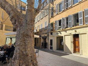 A street with buildings, a tree, and a person standing by a shop. - Le Sainte-Victoire : Studio with beautiful terrace in the to (Aix-en-Provence)