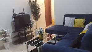 A living room with a blue sofa, a coffee table, a TV, and a potted plant. - Gulf Residency (Nairobi)