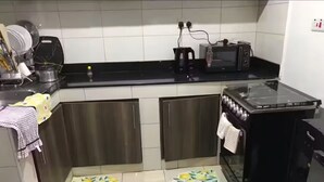 A kitchen with a black countertop, stainless steel cabinets, a black stove, and a refrigerator. There are two small rugs with a lemon pattern on the floor. - Gulf Residency (Nairobi)