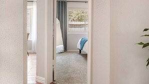 A hallway leading to a bedroom with a window, a door, and a carpeted floor. - The Woodlands Escape | 4 Bedrooms, 2 Baths, Walk to Trails, Near Market Street (Spring)
