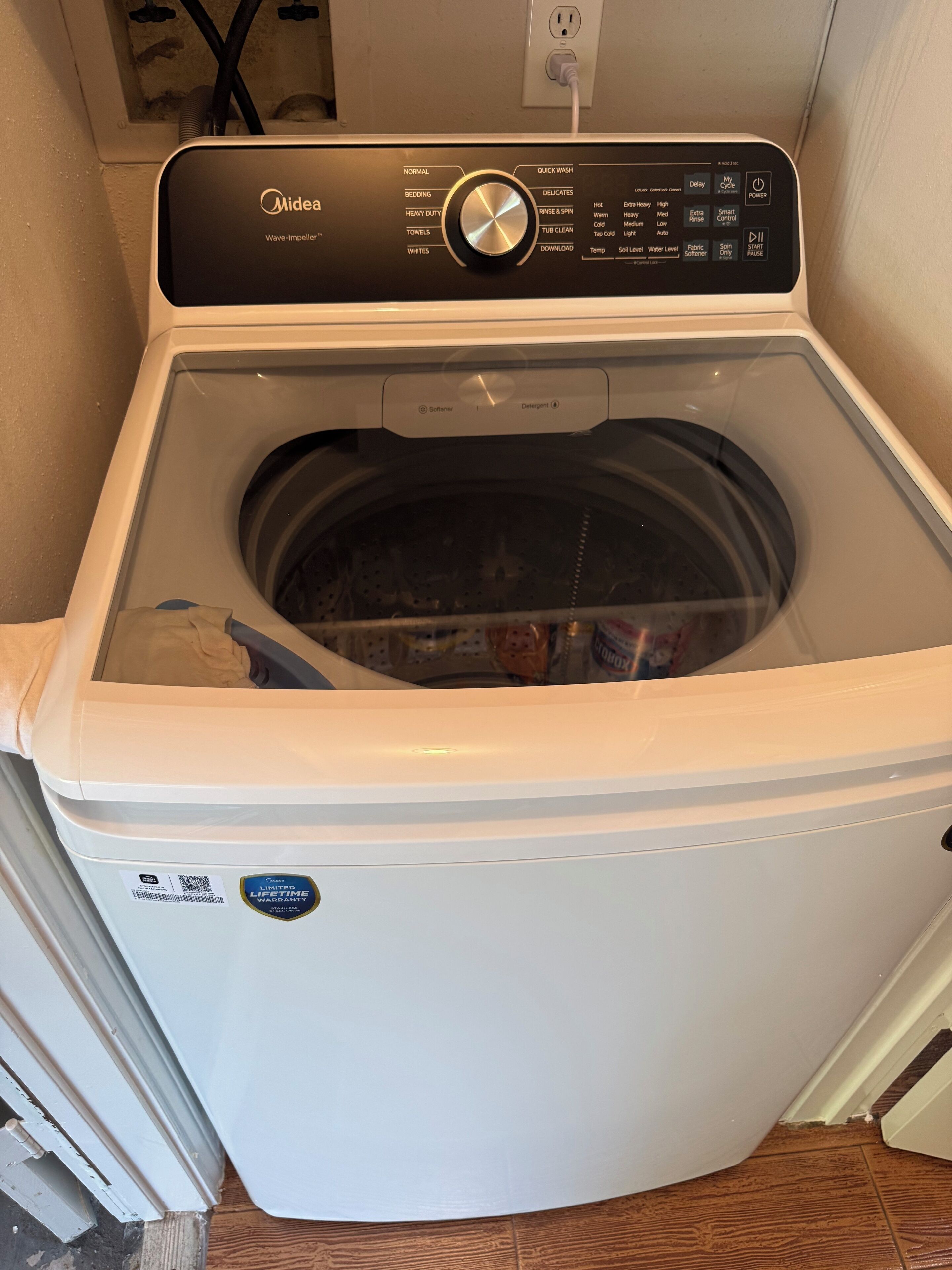 En tvättmaskin från Midea med frontmatning, försedd med en kontrollpanel, ett fack för tvättmedel och en etikett som visar garantitiden.