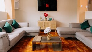 A living room with two grey sofas, a coffee table with a vase of flowers, a TV mounted on the wall, and a cabinet below. - Chabela Host (Cusco)