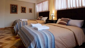 A hotel room with two beds, a headboard, a nightstand, a lamp, and three framed pictures on the wall. - Chabela Host (Cusco)