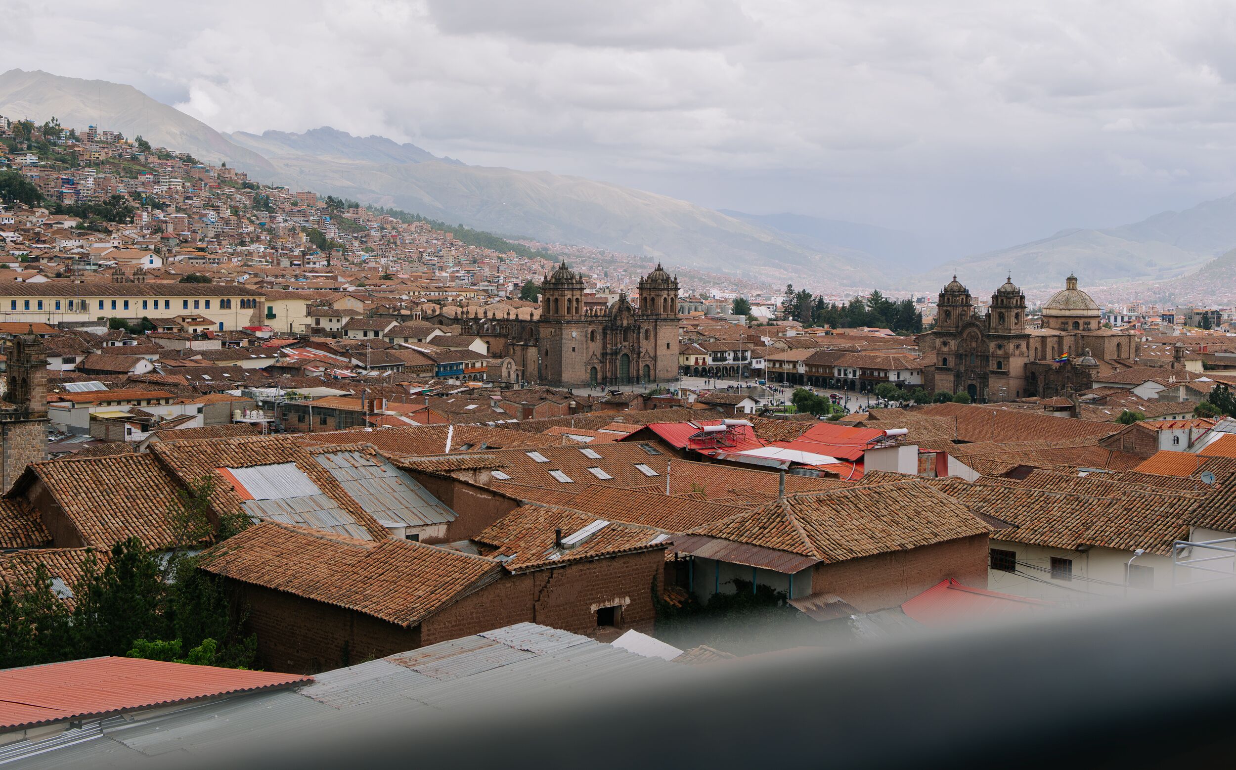 A cityscape with historic architecture, including a prominent cathedral and a bell tower, surrounded by residential buildings with terracotta roofs.