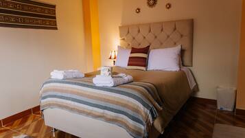 A neatly made bed with a striped blanket and folded towels, a tufted headboard, and a wall-mounted decorative piece.