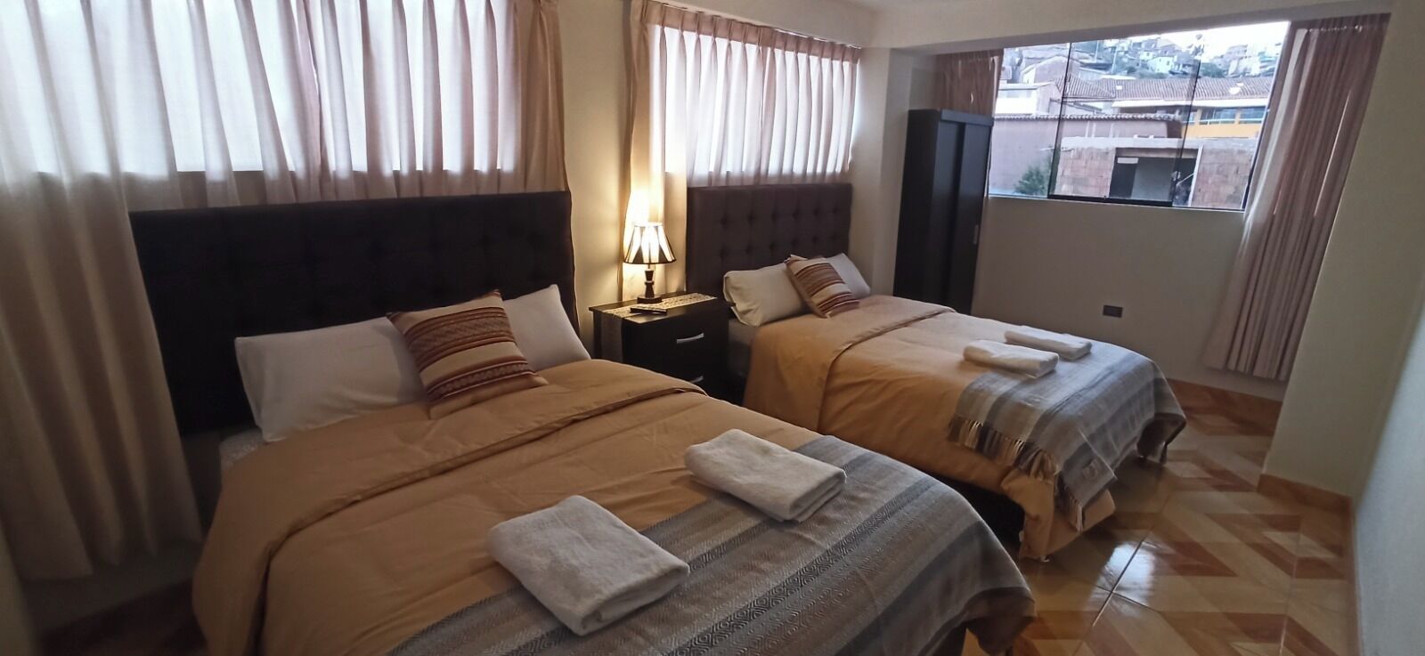 A hotel room with two beds, a nightstand with a lamp, and a window with curtains.