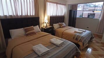 A hotel room with two beds, a nightstand with a lamp, and a window with curtains.