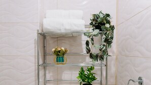 A bathroom with a metal shelf holding white towels, a vase with flowers, and a potted plant. - Chabela Host (Cusco)