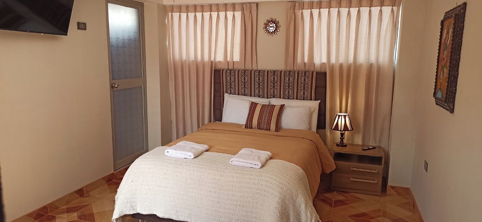 Una cama bien hecha con dos toallas, una lámpara de noche y una mesita de madera.