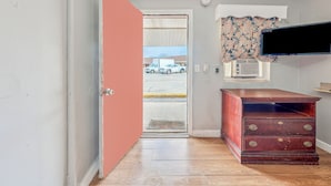 Een kamer met een houten dressoir, een aan de muur bevestigde televisie en een deur die naar buiten leidt.