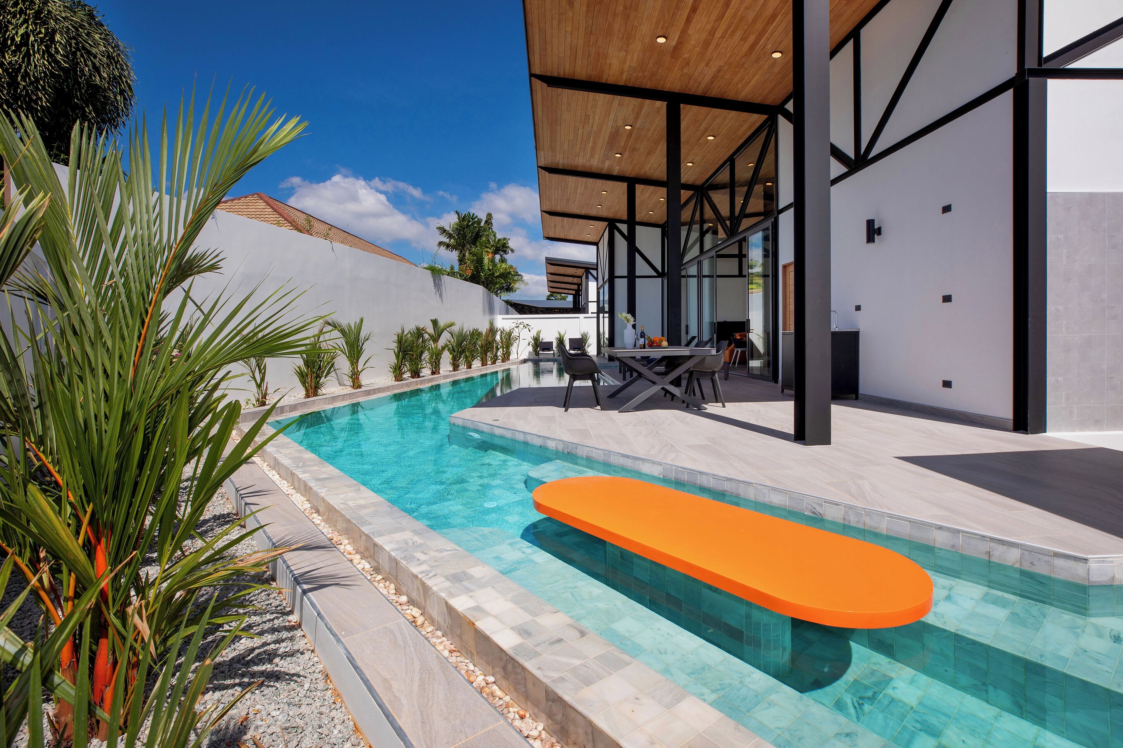 Un espace piscine extérieur moderne, doté d’une terrasse en bois, de sièges et d’une piscine à l’eau d’un bleu cristallin.