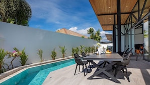 Un espace de restauration extérieur moderne, doté d’une piscine, entouré de plantes et offrant une vue sur un ciel dégagé.