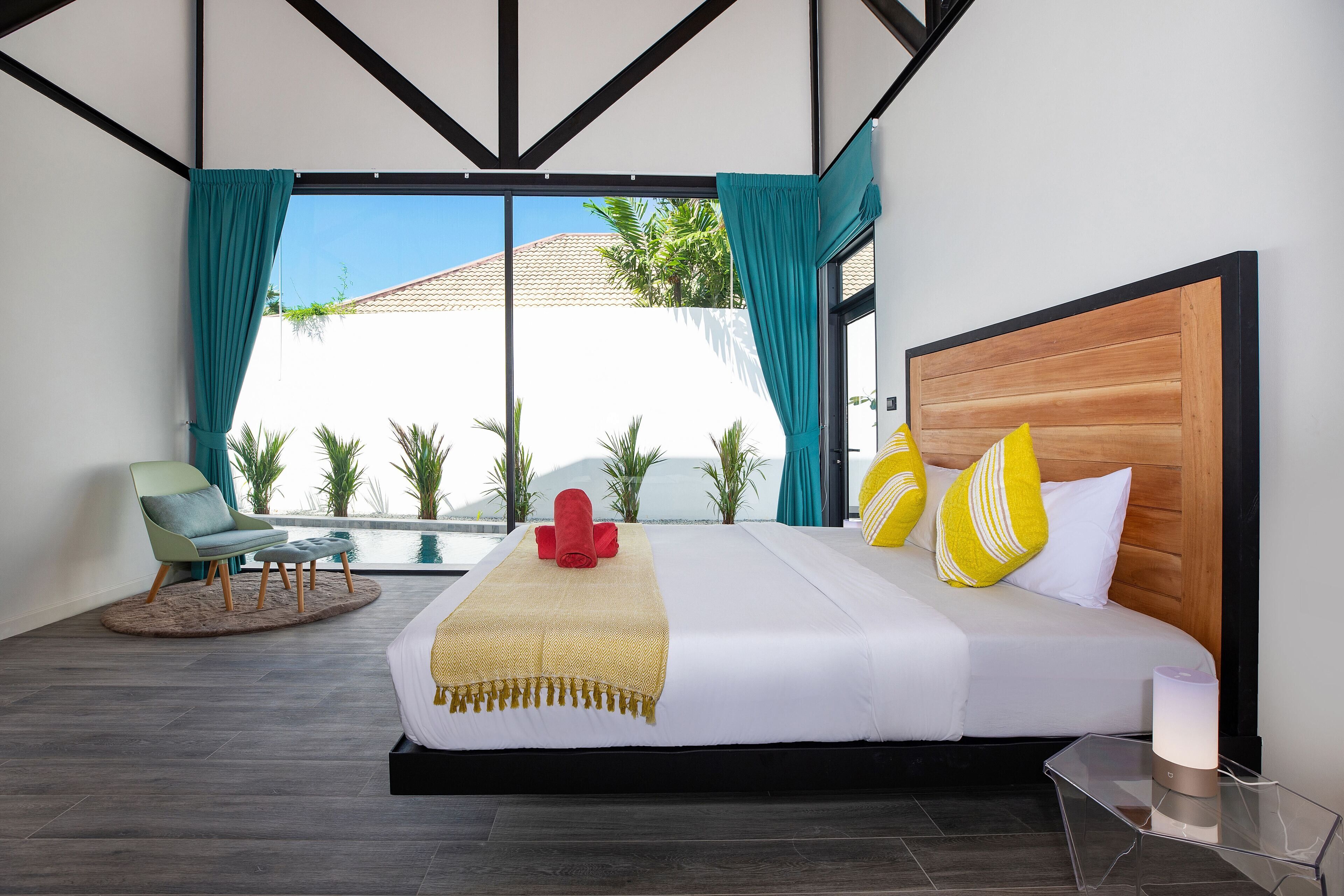 Habitación de hotel moderna con una cama grande, vista a una piscina y una silla junto a la ventana.