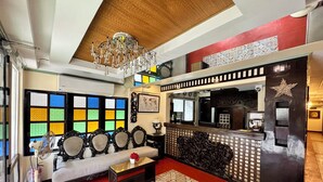 Rebedor d'hotel amb taulell de recepció, un lampadari, un sofà i una finestra colorida.