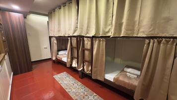 A room with bunk beds, beige curtains, a patterned rug, and a wooden door.