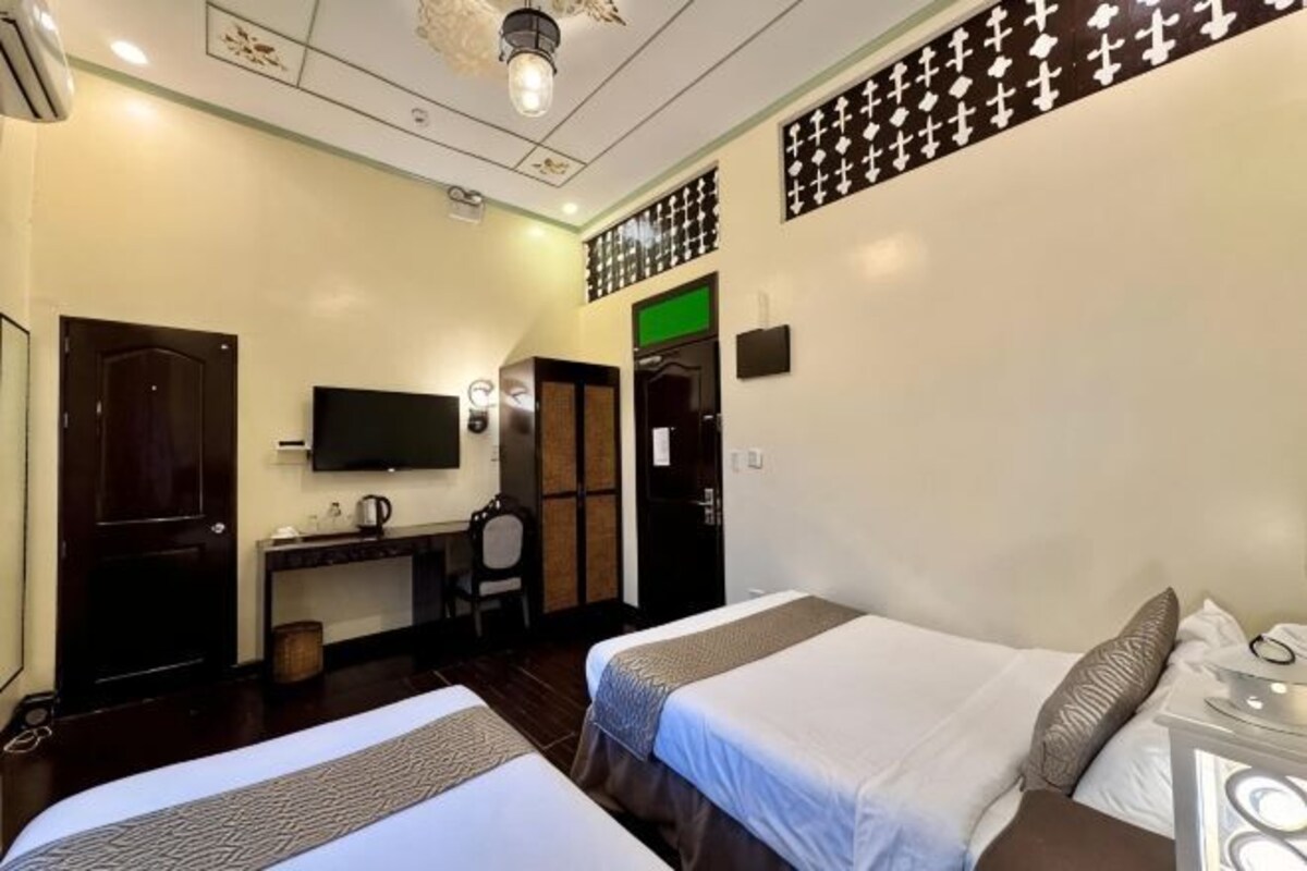 Habitación de hotel con dos camas, un escritorio, una silla, un televisor y una lámpara fijada a la pared.