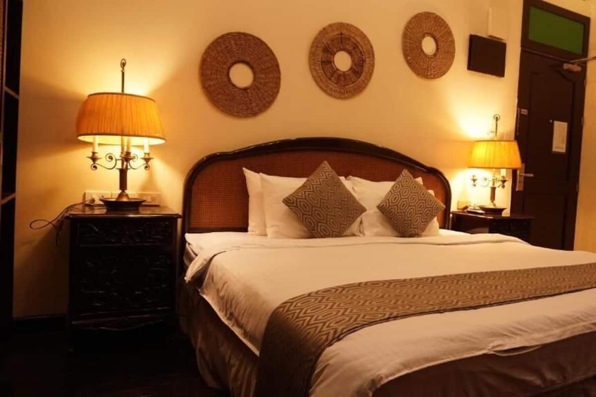Una cama bien hecha con almohadones estampados, dos lámparas de noche y tres adornos circulares en la pared.