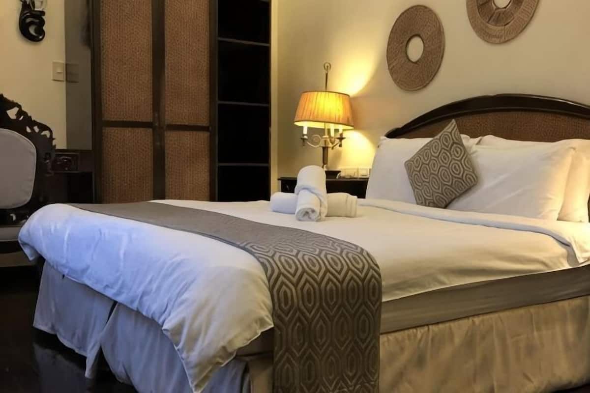 Una cama bien hecha con un cubrecolcha estampado, una lámpara de noche y un reloj de pared.