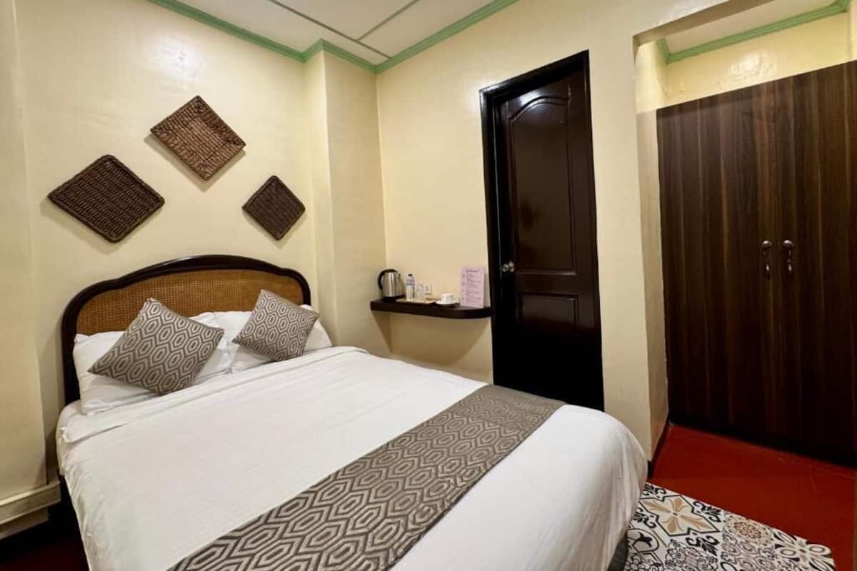 Una habitación de hotel con cama, armario y un pequeño estante con artículos de aseo.