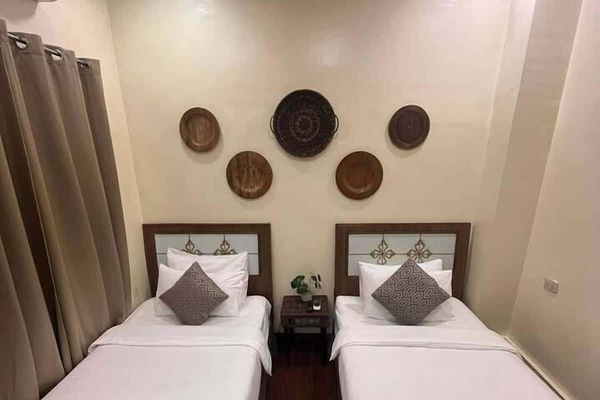 Habitación de hotel con dos camas, una mesita pequeña y una pared decorada con platos.