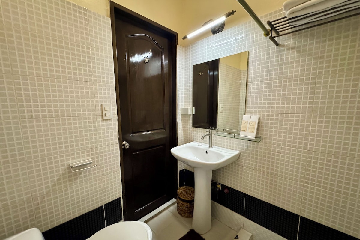 Une salle de bain avec un lavabo blanc, une porte sombre et un miroir au-dessus.