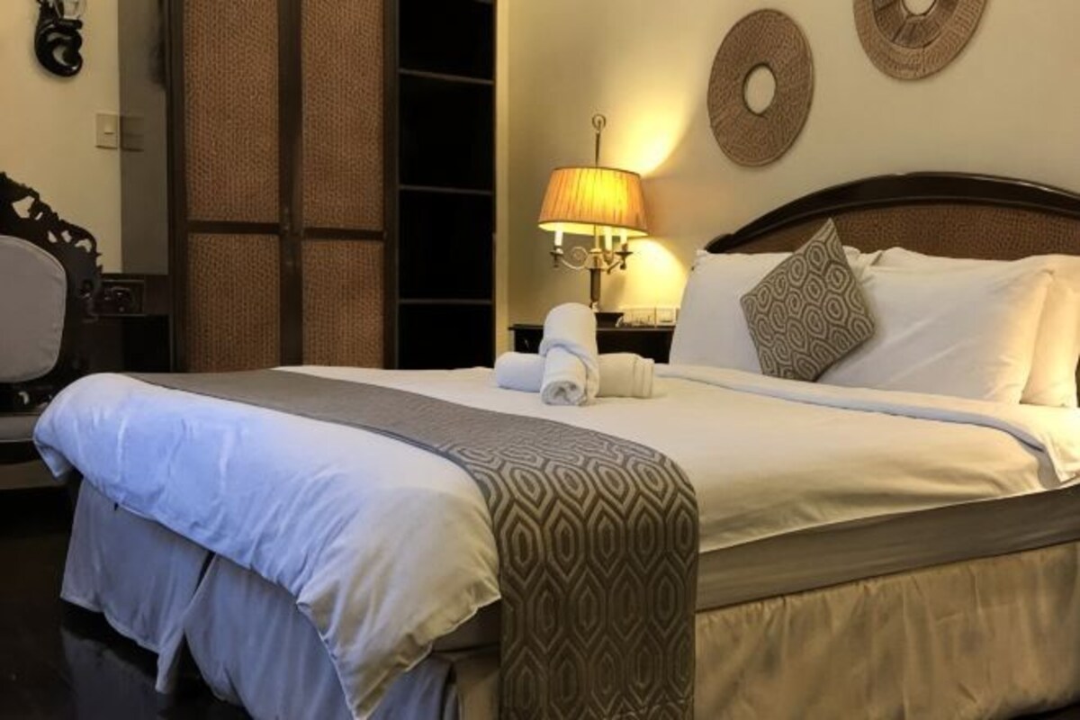 Una cama bien hecha con un cubrecolcha estampado, una lámpara de noche y un reloj de pared.