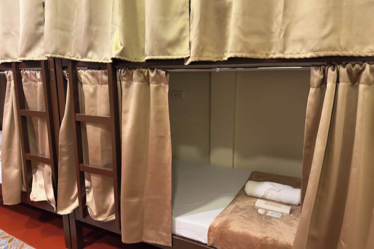 Una cama litera con cortinas, una escalera y una cama bien hecha con una manta marrón.