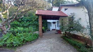 A garden pathway leading to a covered entrance with a red roof, surrounded by lush greenery and potted plants. - Check Inn Today Resort (Coonoor)