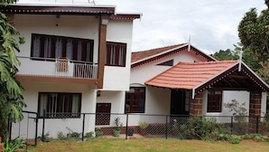 A two-story house with a balcony, a fenced garden, and a red-tiled roof. - Check Inn Today Resort (Coonoor)
