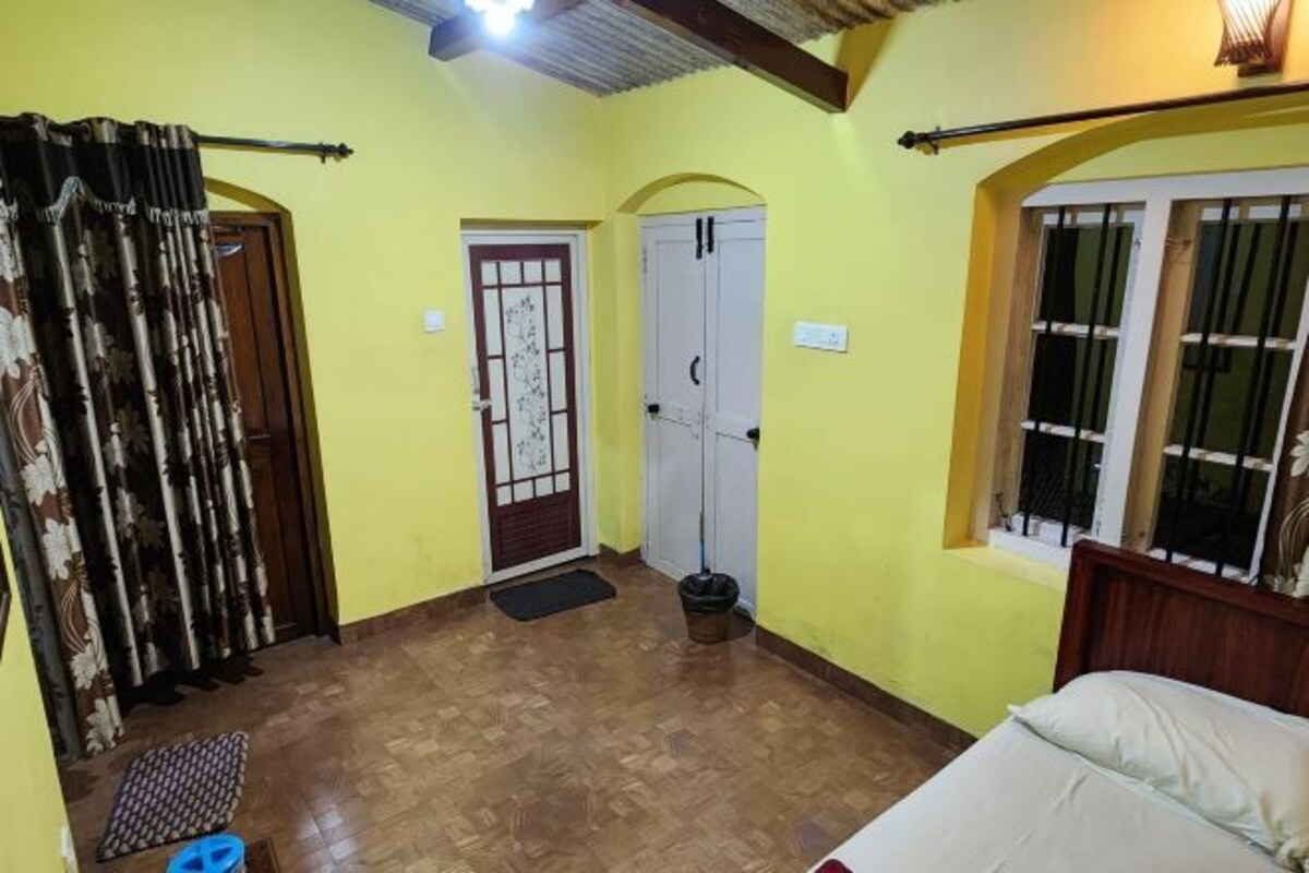 A room with a bed, a window with bars, a door with a decorative glass panel, and a curtain.