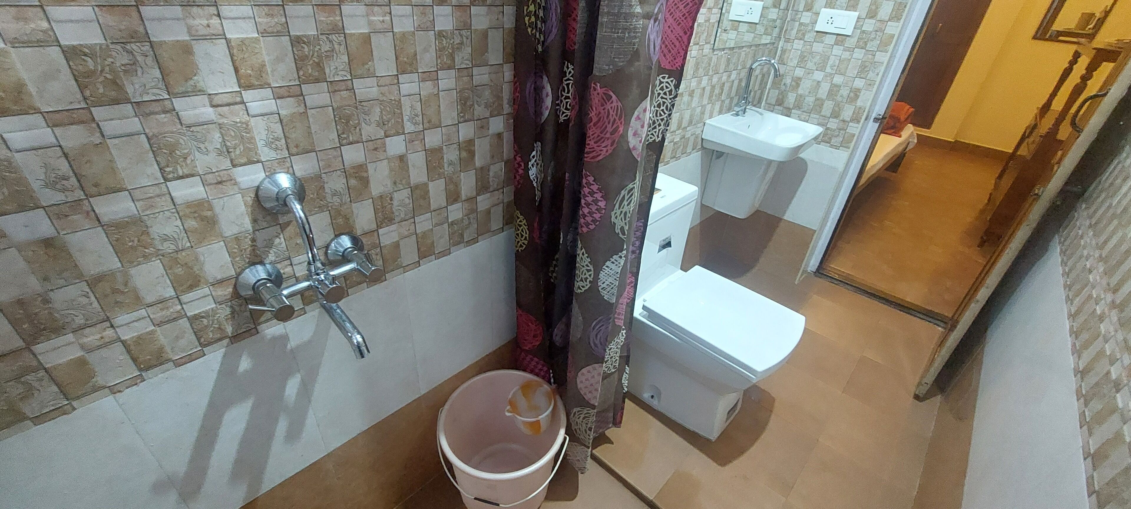 A bathroom with a tiled wall, a sink, a toilet, and a bucket.