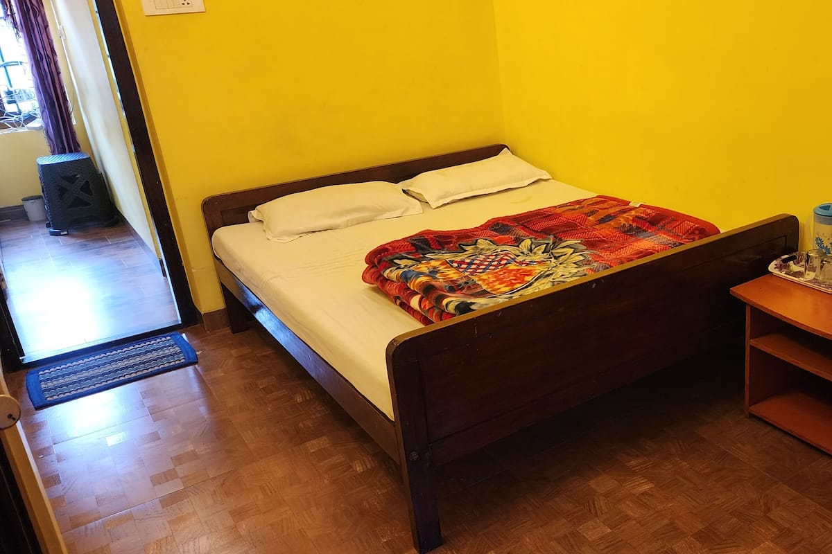 A room with a bed, wooden nightstand, and a small table with a water bottle and glasses.