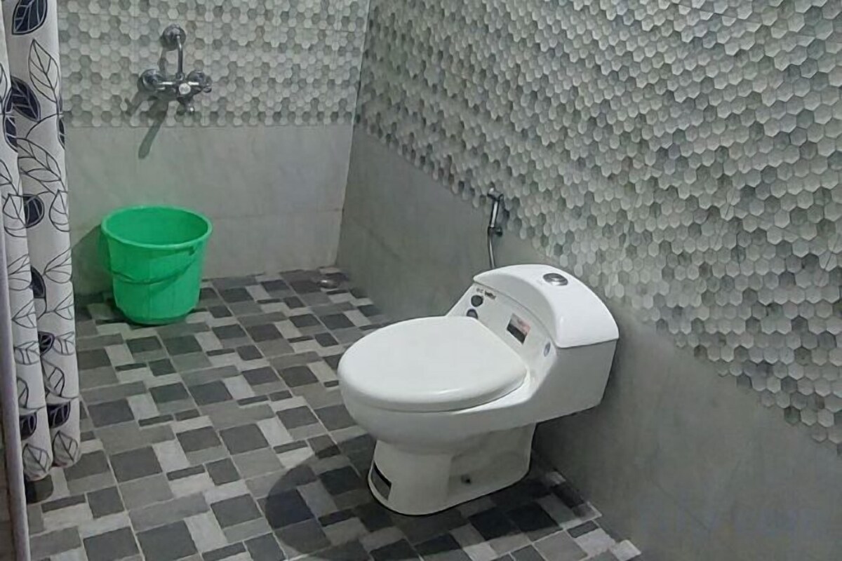 A bathroom with a toilet, a green bucket, and a tiled floor.