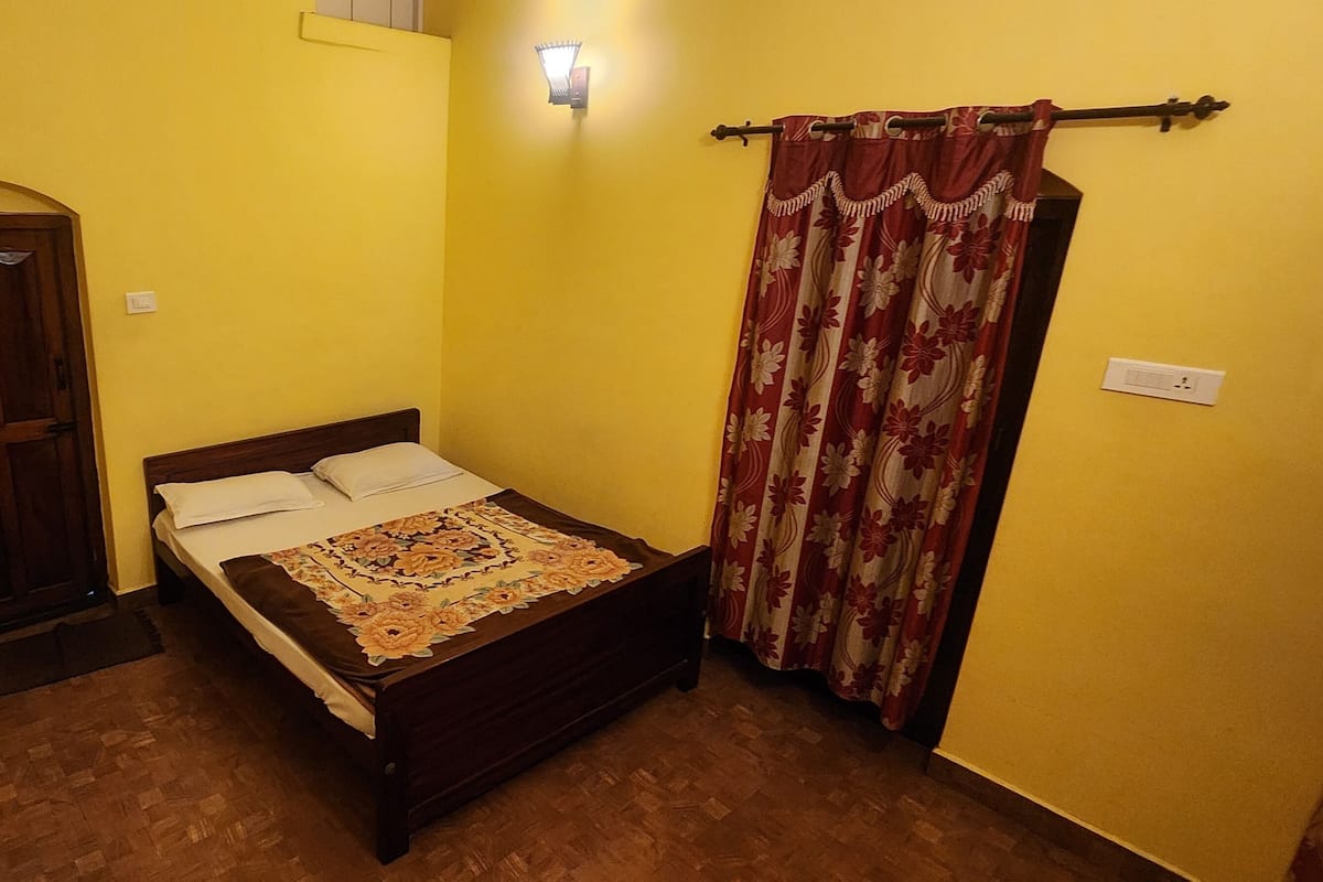 A small, yellow-walled bedroom with a wooden bed, a door, and a curtain.