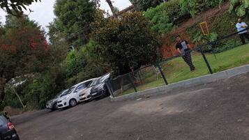 A parking area with several cars, a fence, and greenery.