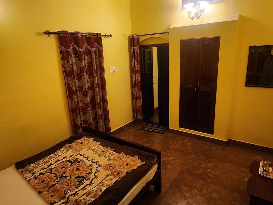 A room with a bed, a small table, a chair, a door, and a wall-mounted light fixture.