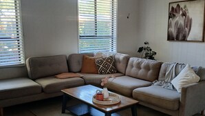 A living room with a sectional sofa, a coffee table, and a large window with blinds.