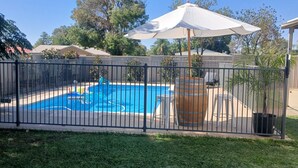 A fenced backyard with a swimming pool, a wooden barrel, and a white umbrella.