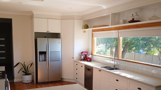 A modern kitchen with white cabinetry, a stainless steel refrigerator, a red mixer, and a window overlooking a backyard.