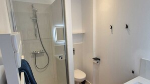 Un baño moderno con ducha de vidrio, inodoro blanco y lavamanos blanco.